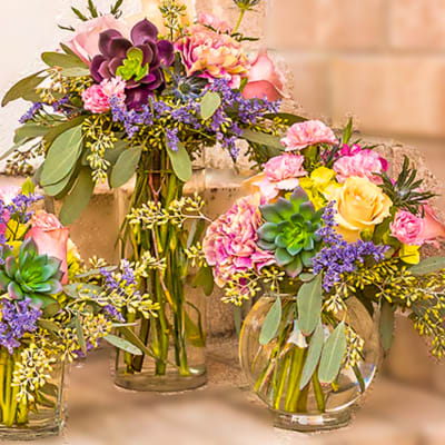 Three colorful floral arrangements in glass vases with succulents