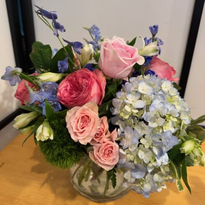 Mixed bouquet of pink roses, blue hydrangea, and blue flowers in a glass vase
