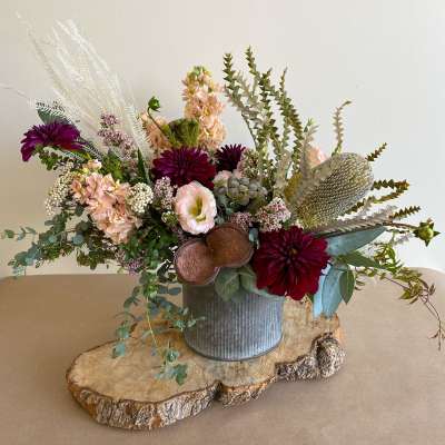 Mixed floral arrangement in a metal bucket on a wood slab