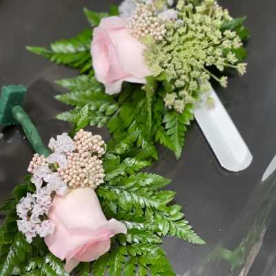Two pink rose boutonnieres with fern and small filler flowers