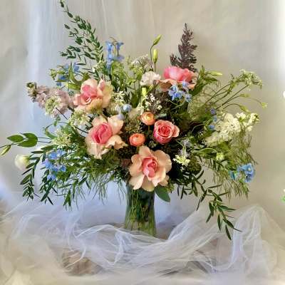Tall mixed bouquet of pink roses and blue flowers in a glass vase