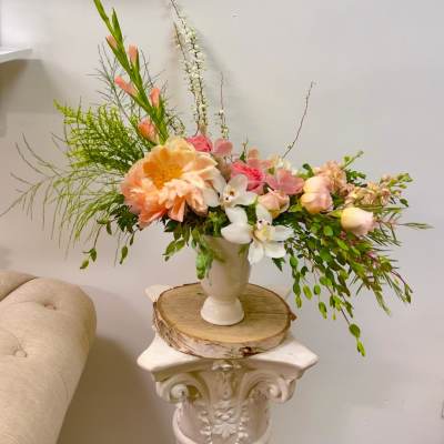 Peach and pink floral arrangement in a white vase on a pedestal