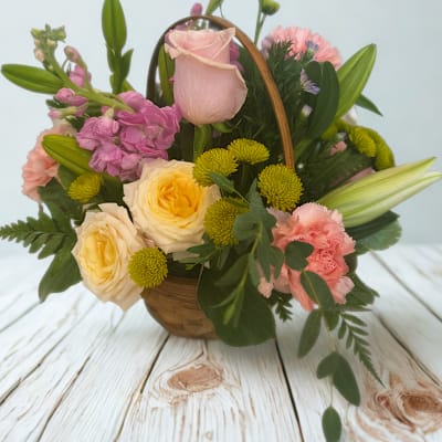 Basket arrangement with pink and yellow roses, lilies, carnations, and small green blooms