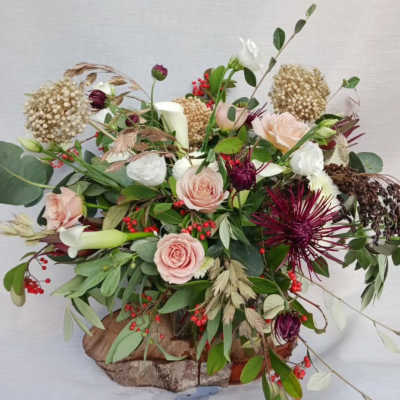 Rustic low arrangement with blush roses, dark red mums, berries, and a candle on a wood base.