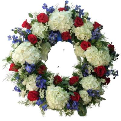 Circular floral wreath with red roses, white hydrangeas, and blue flowers