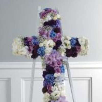 Floral cross arrangement in purple, blue, and white flowers on a stand