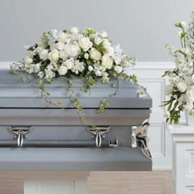 White floral casket spray and standing arrangement beside a gray casket