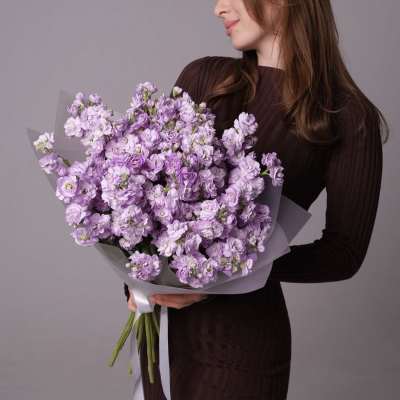 Woman holding a large bouquet of lavender flowers wrapped in gray paper