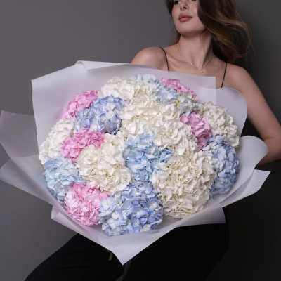 Woman holding a large bouquet of pastel hydrangeas wrapped in white paper