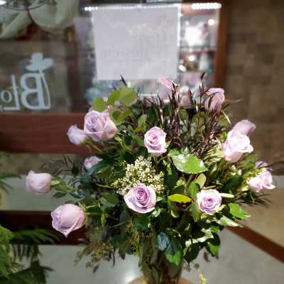 Lavender roses arranged in a glass vase with mixed greenery