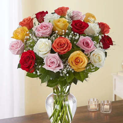 Mixed-color rose bouquet with baby's breath in a clear glass vase on a table.