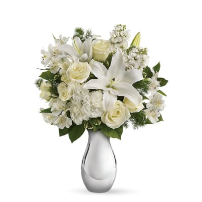Arrangement of white lilies, roses, carnations, and other blooms in a silver vase
