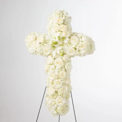 Standing cross-shaped arrangement of white roses, lilies, and hydrangeas on an easel