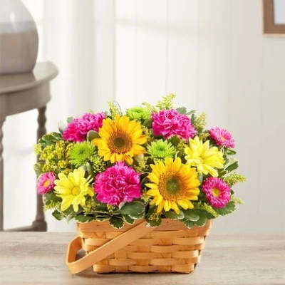 Bright basket arrangement of yellow sunflowers, pink carnations, and yellow and green mums.