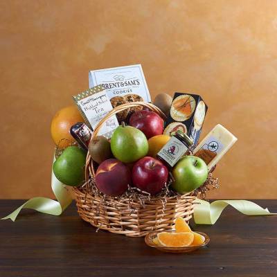 Wicker gift basket filled with assorted fresh fruits and gourmet snacks on a dark table