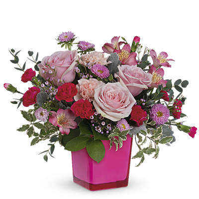 Pink and red mixed flower arrangement with roses and carnations in a bright pink square vase