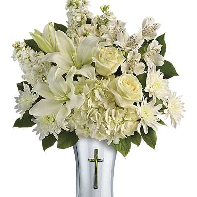 White lilies, roses, and other blooms in a silver vase with a cross cutout.