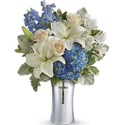White lilies, cream roses, and blue hydrangea in a tall silver vase with a cross cutout