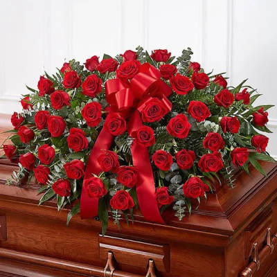 Red rose casket spray with a large red bow on a wooden casket.