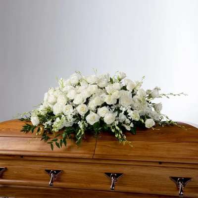 White rose casket spray arrangement resting on a wooden casket