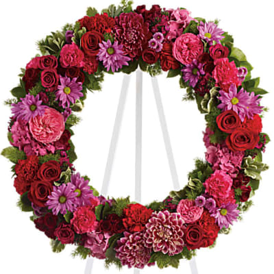 Standing open wreath of red and pink roses, carnations, and mums on a white easel