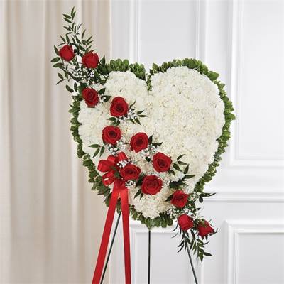 Heart-shaped white floral standing spray with red roses and greenery on an easel.