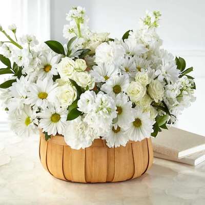 Low basket arrangement of white daisies, roses, and other white blooms on a marble surface