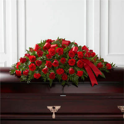Red roses and carnations casket spray with red ribbon on a dark wood casket