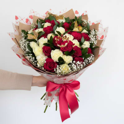 Hand-tied bouquet of red and cream roses with baby's breath wrapped in heart paper and red ribbon