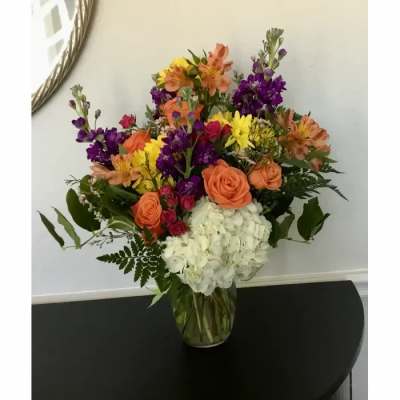 Mixed bouquet of orange, purple, yellow, and white flowers in a clear glass vase
