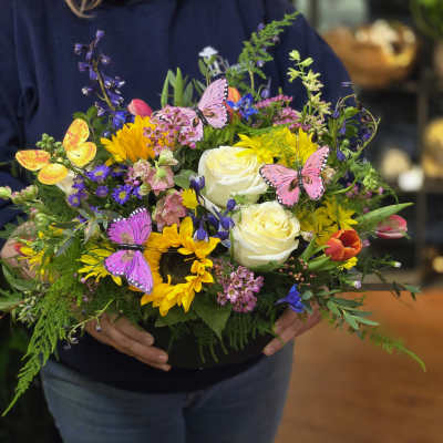 Colorful mixed flower arrangement in a black container with butterfly picks
