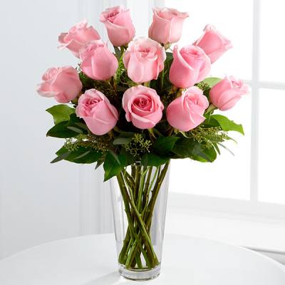 Tall clear glass vase filled with pink roses on a white table