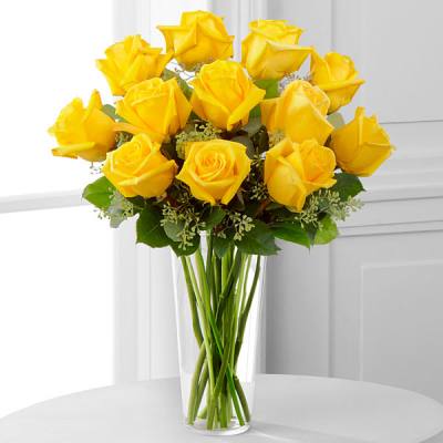 Tall bouquet of yellow roses in a clear glass vase on a white table