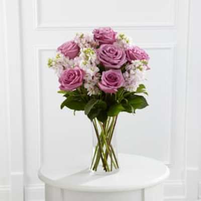 Lavender roses and pale pink blossoms arranged in a clear glass vase