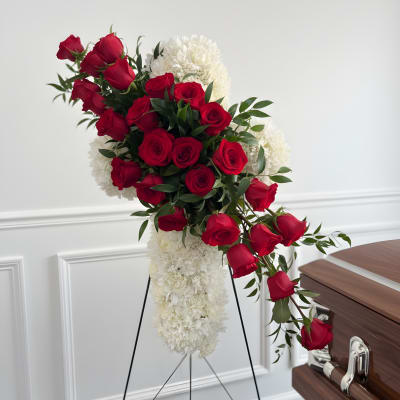 Red roses and white flowers arranged on a standing easel beside a casket