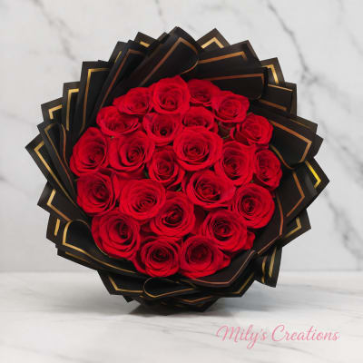 Round bouquet of red roses wrapped in black and gold paper on a marble surface