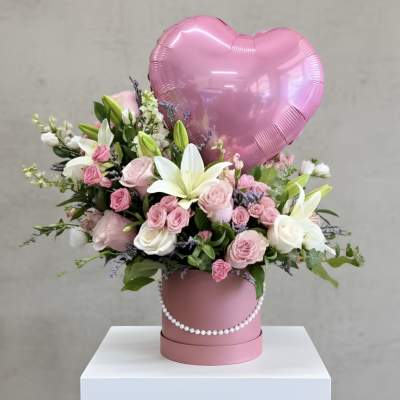 Pink heart balloon above a pink flower box with roses and lilies