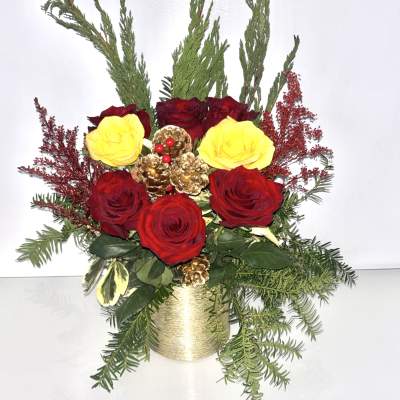 Red and yellow roses in a gold container with evergreen accents