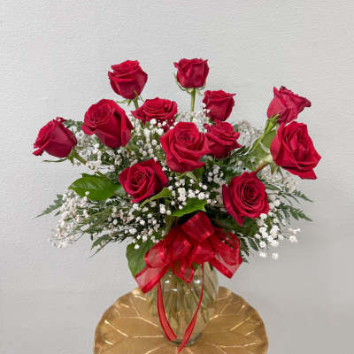 Red roses arranged in a glass vase with baby's breath and a red ribbon