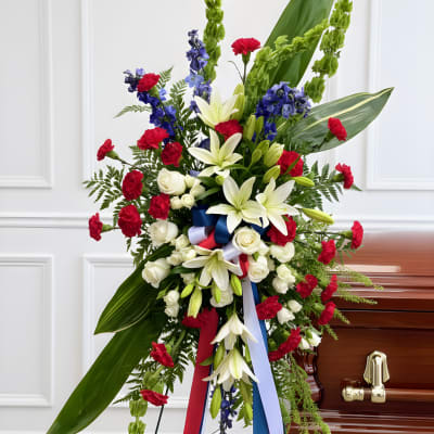Standing funeral spray with white lilies, red carnations, and blue flowers