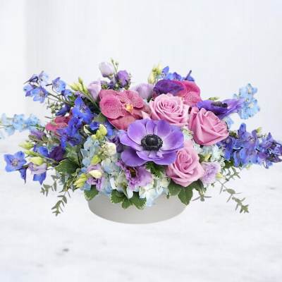 Pink and purple mixed flower arrangement in a white bowl vase