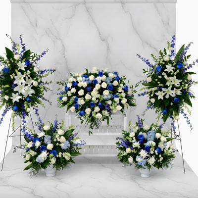 Blue and white floral funeral display with standing sprays and vase arrangements