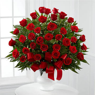 Red roses arranged in a white vase with a red ribbon