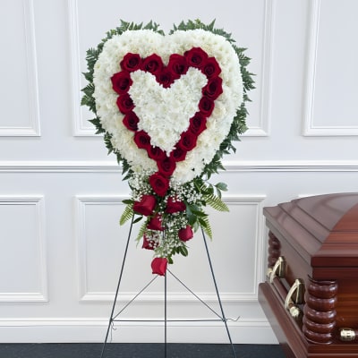 Heart-shaped funeral spray of white flowers and red roses beside a casket