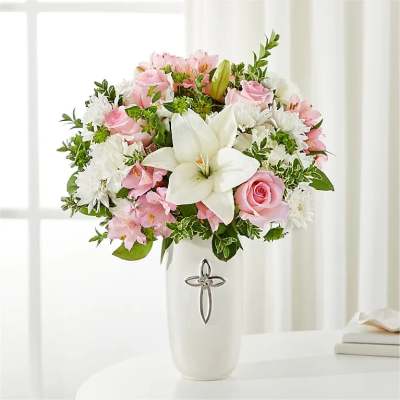 Pink and white flower arrangement in a white vase with a cross