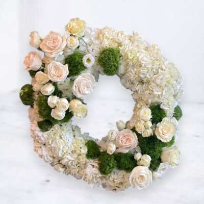 Circular floral wreath with white hydrangeas, cream roses, and green moss accents