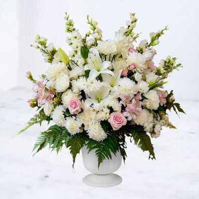 Large white and pink floral arrangement with lilies, roses, and mums in a white pedestal vase