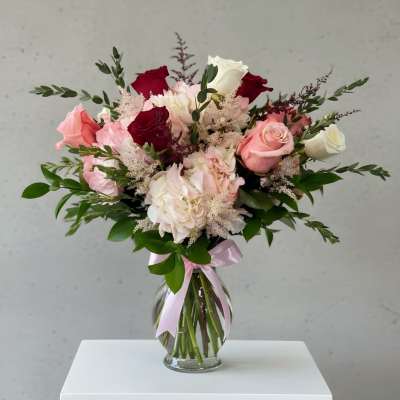 Pink and red rose bouquet in a clear glass vase with a ribbon