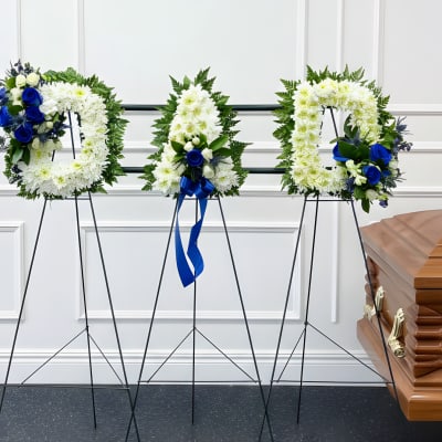 Three funeral wreaths on stands beside a casket