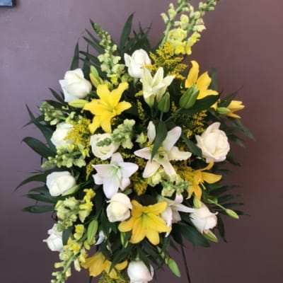 Standing floral spray with white roses and yellow lilies on a metal easel